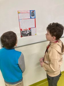 Dwóch uczniów klasy czwartek stoi przed białą tablicą i przygląda się plakatowi zatytułowanemu "Noblista Lech Wałęsa".