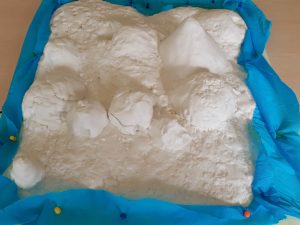 Zdjęcie przygotowanego podłoża do makiety zimowej krainy. Na niebieskim podłożu, biała nierówna forma tworząca góry i doliny.