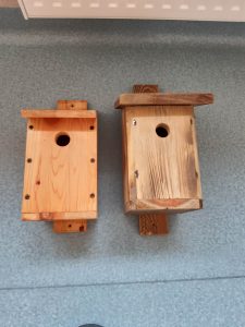 Zdjęcie leżących na podłodze dwóch drewnianych karmników. Oba mają okrągłe otwory.