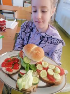 Uczennica klasy trzeciej trzyma tacę z kanapkami na których poukładane są warzywa.