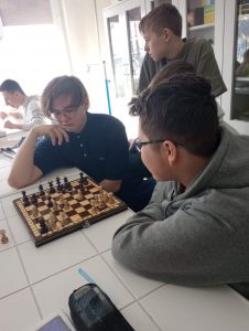 Uczniowie klasy ósmej podczas gry w szachy. Na zdjęciu widoczny jest chłopiec podpierający głowę o dłoń i zastanawiający się nad kolejnym ruchem.