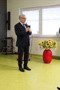 Starosta toruński stoi z mikrofonem obok niego na ziemi stoi ustawiony czerwony wazon z żółtymi słonecznikami.