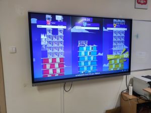 Zdjęcie monitora zawieszonego na ścianie na którym wyświetla się rozwiązywany przez uczniów quiz.