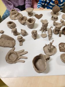 Zdjęcia ustawionych na stole glinianych figurek wykonanych przez uczniów podczas warsztatów.