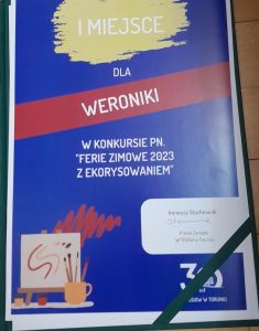 Zdjęcie dyplomu. Na niebieskim tle napisy: "I MIEJSCE DLA WERONIKI W KONKURSIE PN. "FERIE ZIMOWE 2023 Z EKORYSOWANIEM". Poniżej w białej ramce podpis Prezesa Zarządu WFOŚiGW w Toruniu Ireneusza Stachowskiego. Na dole dyplomu grafika przedstawiająca kartkę i przybory plastyczne.