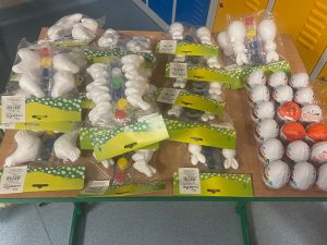 Zdjęcie otrzymanych przez uczniów nagród w konkursie. Na stoliku leżą ułożone kinder niespodzianki oraz opakowania z białymi kurczaczkami i króliczkami do malowania.