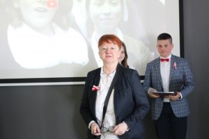 Pani Wiesława Urbańska przygotowujaca apel podczas przemówienia rozpoczynającego spotkanie. W tle widać jednego z uczniów klasy ósmej prowadzącego apel.