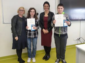 Dwoje zwycięzców w konkursie pozuje do wspólnego zdjęcia wraz z Panią Dyrektor i nauczycielką religii. Uczniowie trzymają przed sobą otrzymane dyplomy.