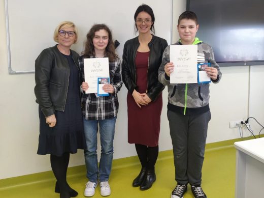 Dwoje zwycięzców w konkursie pozuje do wspólnego zdjęcia wraz z Panią Dyrektor i nauczycielką religii. Uczniowie trzymają przed sobą otrzymane dyplomy.