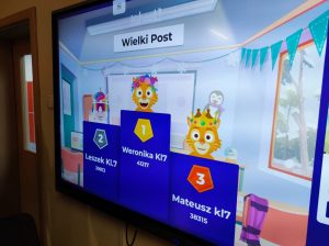 Zdjęcie tablicy multimedialnej, na której wyświetlona jest grafika z wynikami w konkursie. Nad trzema prostokątami różnej wysokości umieszczone są grafiki zwierzątek. Na prostokątach napisy od lewej strony: "2 Leszek kl.7 39813", "1 Weronika kl 7 41217" oraz "3 Mateusz kl7 38315".