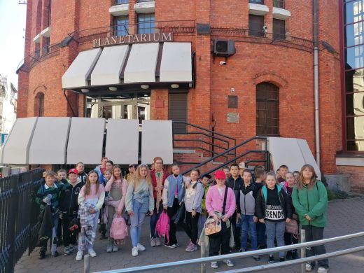 Uczniowie klasy trzeciej i czwartej pozują do grupowego zdjęcia przed budynkiem planetarium w Toruniu.
