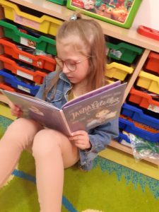 Uczennica siedzi na podłodze i czyta książkę.