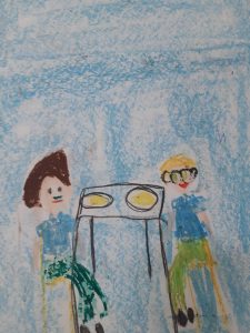 Zdjęcie rysunku wykonanego przez ucznia oddziału przedszkolnego kredkami. Rysunek przedstawia dwie postacie siedzące przy stole.