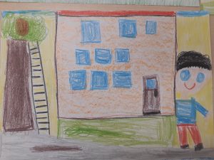Zdjęcie rysunku wykonanego przez ucznia oddziału przedszkolnego kredkami. Rysunek przedstawia dom i stojącego obok chłopca.