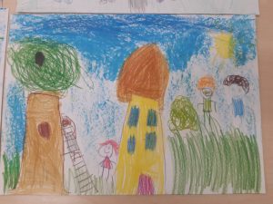 Zdjęcie rysunku wykonanego przez ucznia oddziału przedszkolnego kredkami. Rysunek przedstawia dom i stojące obok postacie. Jedna z nich wspina się po drabinie opartej o drzewo stojące obok domu.