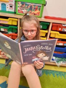 Uczennica siedzi na podłodze i czyta książkę.