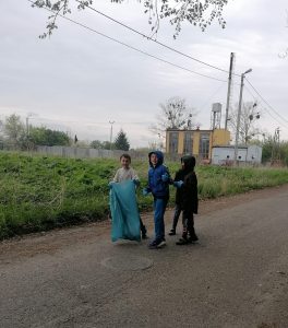 Trzech uczniów w gumowych rękawiczkach idzie gruntową drogą z dużym workiem na śmieci.
