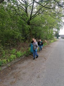 Troje uczniów klasy trzeciej idzie drogą trzymając duży worek na śmieci.