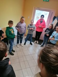 Uczniowie klasy trzeciej stoją w kręgu wraz z Panią bibliotekarką. Zdjęcie wykonane w gminnej bibliotece w Ostaszewie.