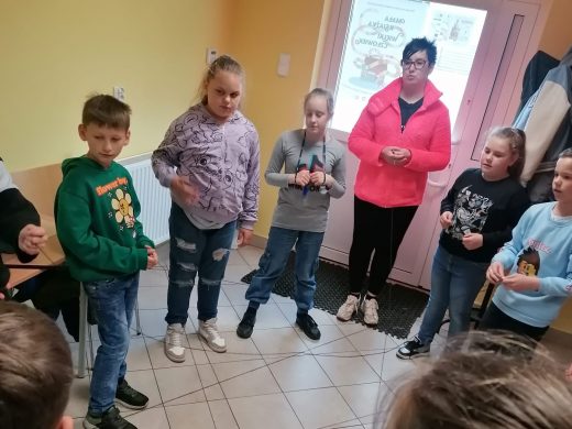 Uczniowie klasy trzeciej stoją w kręgu wraz z Panią bibliotekarką. Zdjęcie wykonane w gminnej bibliotece w Ostaszewie.