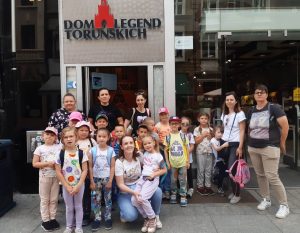 Uczniowie wraz z mamami pozują do wspólnego zdjęcia przed budynkiem z szyldem "DOM LEGEND TORUŃSKICH".