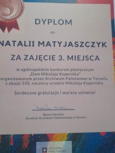 Zdjęcie otrzymanego przez Natalię Matyjaszczyk dyplomu. Na białym tle różnej wielkości napisy: "DYPLOM dla NATALII MATYJASZCZYK ZA ZAJĘCIE 3. MIEJSCA w ogólnopolskim konkursie plastycznym 'Dom Mikołaja Kopernika" zorganizowanym przez Archiwum Państwowe w Toruniu z okazji 550. rocznicy urodzin Mikołaja Kopernika. Serdeczne gratulacje i wyrazy uznania ! Beata Herdzin Dyrektor Archiwum Państwowego w Toruniu."