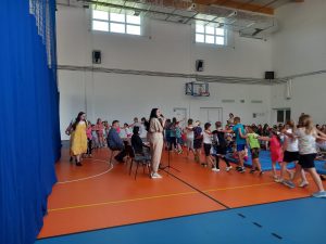 Uczniowie pod przewodnictwem Pani w żółtej sukience utworzyli długi wąż, który zakręca wokół muzyków z Toruńskiej Orkiestry Symfonicznej.