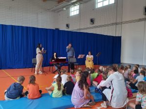 Czworo muzyków z Toruńskiej Orkiestry Symfonicznej stoi przed uczniami siedzącymi na materacach.