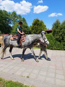 Uczeń siedzi na koniu prowadzonym przez jego opiekuna.