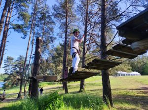 Uczennica w kasku idzie po zawieszoną nad ziemią kładką. Dziewczynka dłoniami trzyma się liny.