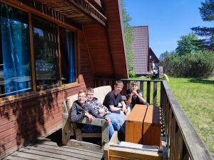 Czworo uczniów siedzi na kanapie na ganku drewnianego domku. Chłopcy się uśmiechają.