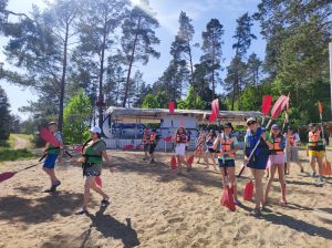 Uczniowie ubrani w kapoki z wiosłami idą po plaży.