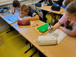 Uczniowie klasy czwartej siedzą przy wspólnym stole i wykonują zadania z okazji Dnia Kropki. Przed dziećmi leżą kartki z kolorowymi kropkami.