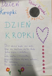 Kartka papieru ozdobionego kolorowymi napisami "Dzień Kropki" oraz z tekstem wiersza ułożonym przez uczennice o treści: "Dziś dzień kropki moi mili, Więc nie martwcie się bez chwili, Jestem piękna i malutka, Taka sprytna i czarniutka, Więc, nie bójcie się mnie wstawiać, Bez wahania, Piszcie mnie na końcu zdania.".