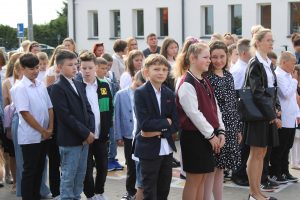 Uczniowie stoją w biało czarnych stroją na szkolnym boisku przed wejściem do szkoły.
