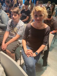 Uczeń wraz z nauczycielką siedzą na krzesłach podczas spotkania motywacyjnego matma^2. Nauczycielka uśmiecha się.