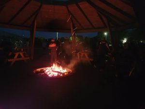 Zdjęcie ogniska palącego się nocą. Za ogniskiem stoi jeden uczeń.