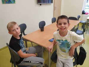 Dwóch uczniów siedzących przy stole na szkolnej stołówce szeroko uśmiecha się do zdjęcia.