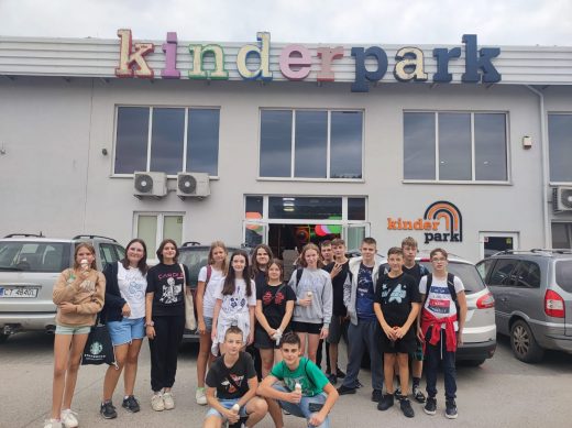 Uczniowie klasy siódmej pozują do wspólnego zdjęcia przed budynkiem z kolorowym napisem "kinderpark". Dzieci trzymają w dłoniach lody.