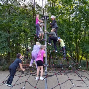 Uczniowie oddziału przedszkolnego wspinają się po drabince w kształcie stożka ustawionej na placu zabaw.