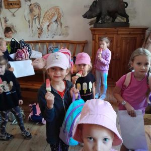 Uczniowie oddziału przedszkolnego stoją w budynku leśniczówki. Dzieci jedzą lody w kształcie arbuzów.