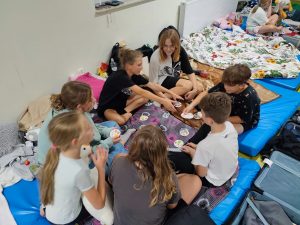 Uczniowie klasy VI siedzą w kółku na materacach i grają w grę. Rozkładają przed sobą kolorowe kółka