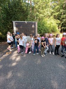 Uczniowie stoją w rzędzie odwróceni plecami do pomnika z napisem "MIEJSCE PAMIĘCI NARODOWEJ BARBARKA".