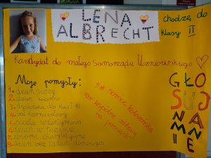 Zdjęcie plakatu ucznia biorącego udział w wyborach do samorządu uczniowskiego. Na żółtym tle po lewej stronie zdjęcie dziewczynki. Obok napis "LENA ALBRECHT" chodzę do klasy II". Poniżej napisy: "Kandydat do małego Samorządu Uczniowskiego"; "Moje pomysły: 1. dzień pizzy 2. dzień kolorów 3. dyskoteka dla klas I -III 4. bal karnawałowy 5. poczta walentynkowa 6. dzień w piżamie 7. zbiórki charytatywne 8. dzień bez zadań domowych 9. pomoc koleżeńska 10. wspólne zabawy na przerwach" oraz po prawej stronie większy napis: "GŁOSUJ NA MNIE".