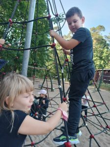 Uczeń wspina się po siatce na placu zabaw. Patrzy na znajdującą się niżej koleżankę.