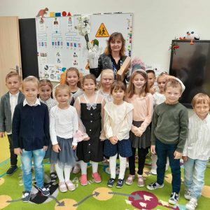 Uczniowie oddziału przedszkolnego pozują do wspólnego zdjęcia z wychowawczynią. Pani trzyma otrzymane przez dzieci upominki.