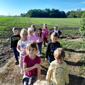 Uczniowie oddziału przedszkolnego idą ubitą drogą. Za nimi widać lekko zielone pole.