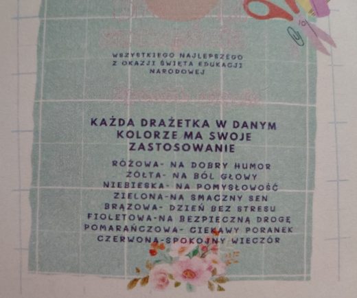 Zdjęcie karteczki z życzeniami dołączonej do prezentów. Na pistacjowym tle w białą kratę napis: "WSZYSTKIEGO NAJLEPSZEGO Z OKAZJI DNIA EDUKACJI NARODOWEJ" . Poniżej większą czcionką napis: "KAŻDA DRAŻETKA W DANYM KOLORZE MA SWOJE ZASTOSOWANIE" i mniejszą czcionką dodane: "RÓŻOWA - NA DOBRY HUMOR ŻÓŁTA - NA BÓL GŁOWY NIEBIESKA - NA POMYSŁOWOŚĆ ZIELONA - NA SMACZNY SEN BRĄZOWA -DZIEŃ BEZ STRESU FIOLETOWA - NA BEZPIECZNĄ DROGĘ POMARAŃCZOWA - CIEKAWY PORANEK CZERWONA - SPOKOJNY WIECZÓR". U dołu grafika z jasno-różowymi kwiatami.