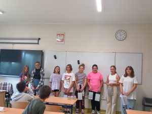 Uczennice klasy piątej stoją w rzędzie pod tablicą. W dłoniach trzymają torebki z prezentami dla chłopców.