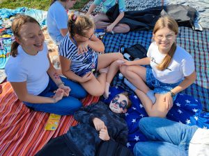 Uczennice klasy szóstej siedzą w siadzie skrzyżnym na kocach. Przed nimi leży ich kolega z maseczką pandy na twarzy.